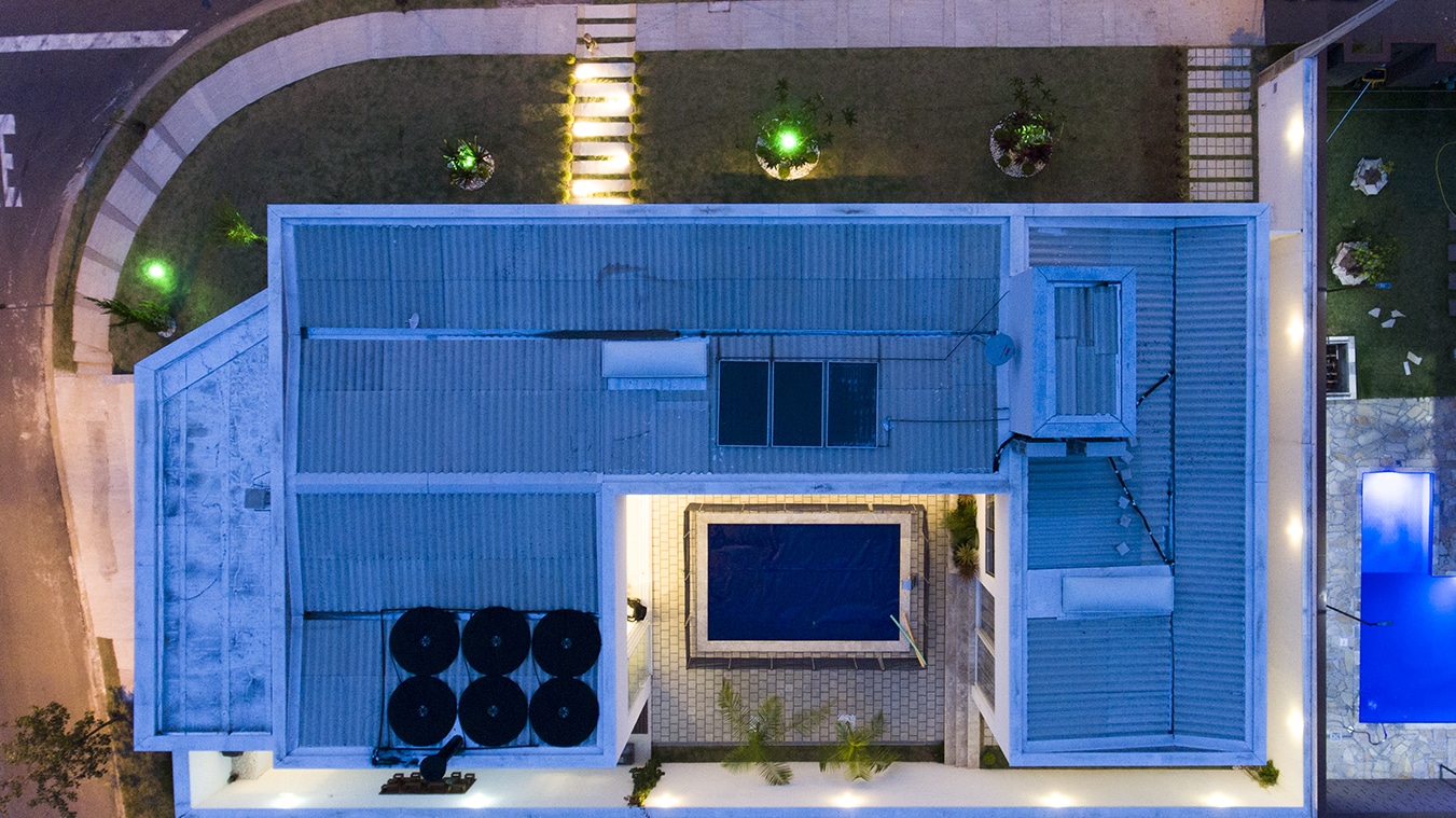 foto aerea noturna é possivel perceber a iluminação da casa e da área da piscina além dos detalhes do telhado