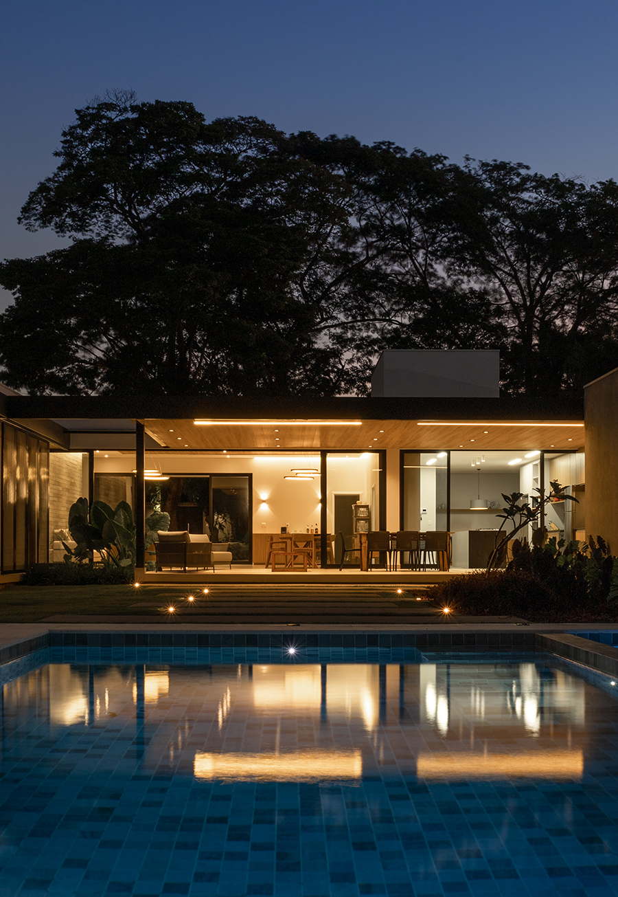 vista noturna dos fundos da casa com destaque para a piscina e beiral em estrutura metálica com forro de madeira