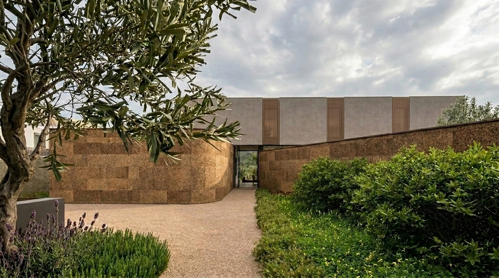 Entrada principal de residência contemporânea em Portugal com paredes curvas revestidas em cortiça natural e paisagismo mediterrânico.